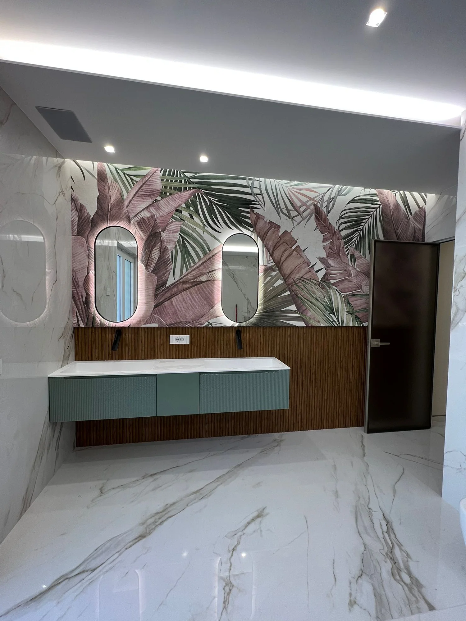 Bagno realizzato con doppio lavabo verde, specchi ovali e rivestimento botanico.