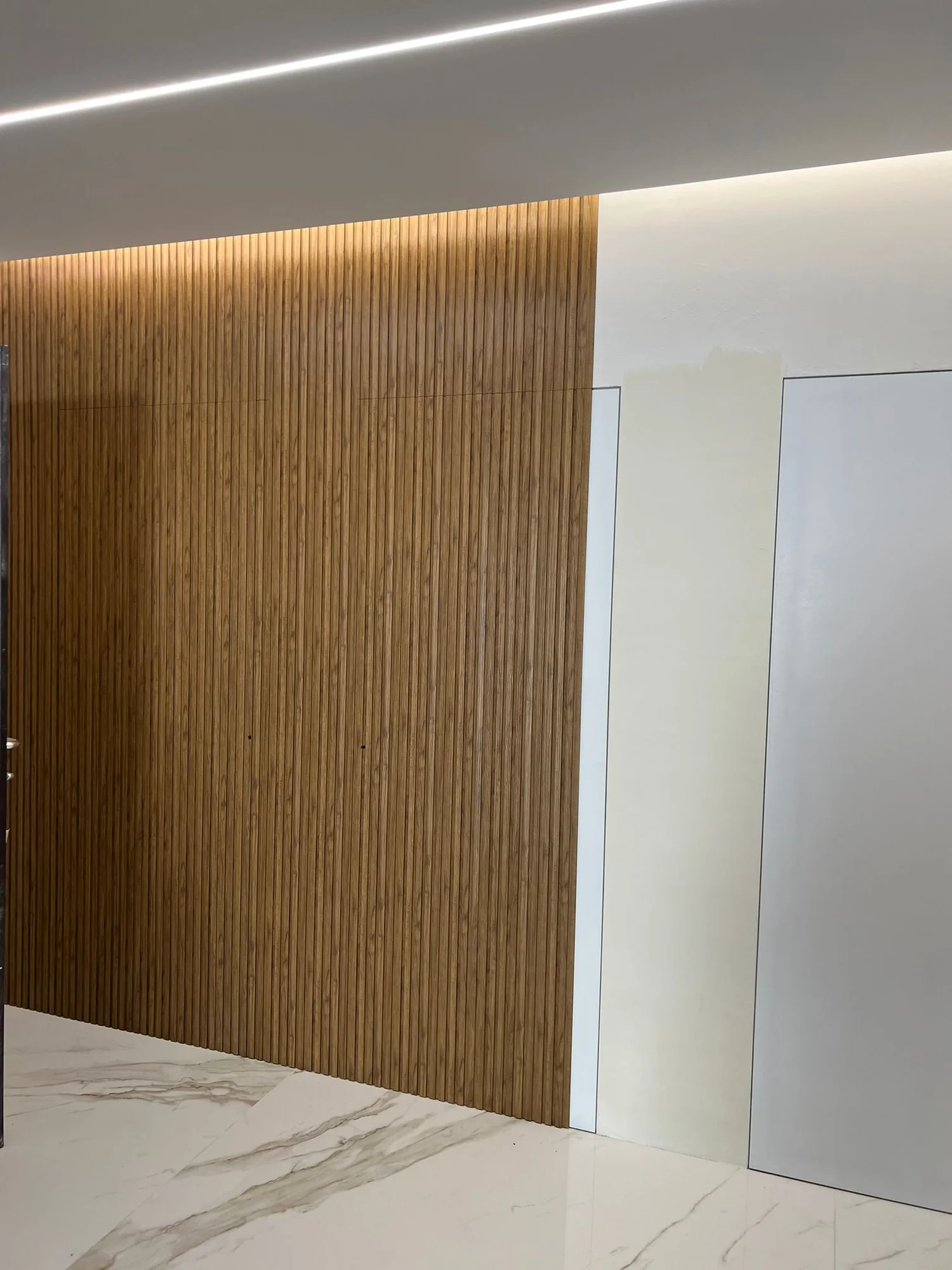 Boiserie a listelli in legno con illuminazione radente e porte a filo parete.